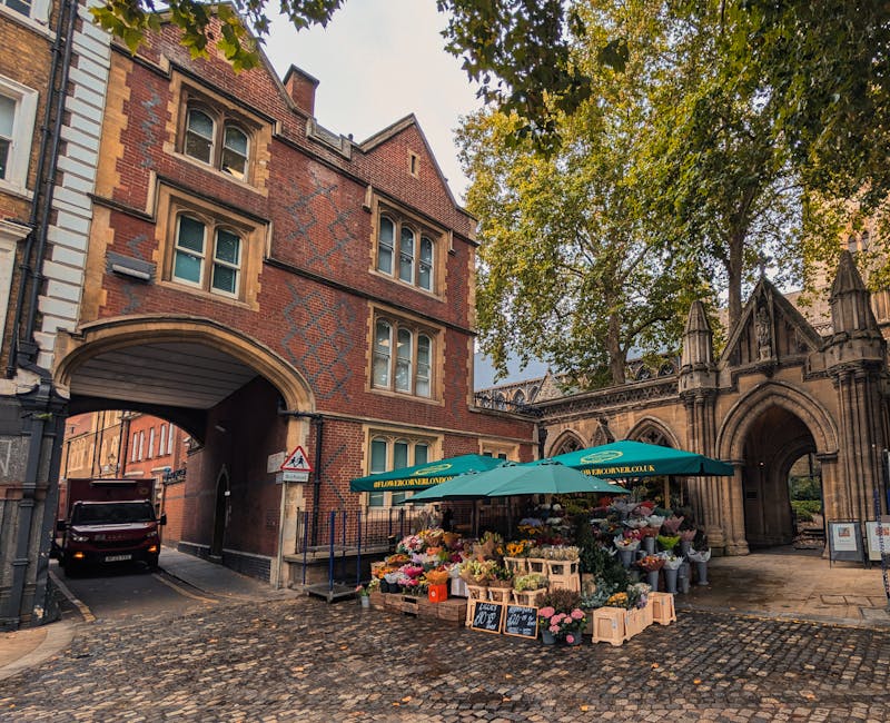 A vibrant flower stall under a green umbrella located on a cobblestone street near Catford Bridge Station SE6, with an assortment of fresh flowers including roses, tulips, and daisies in various color